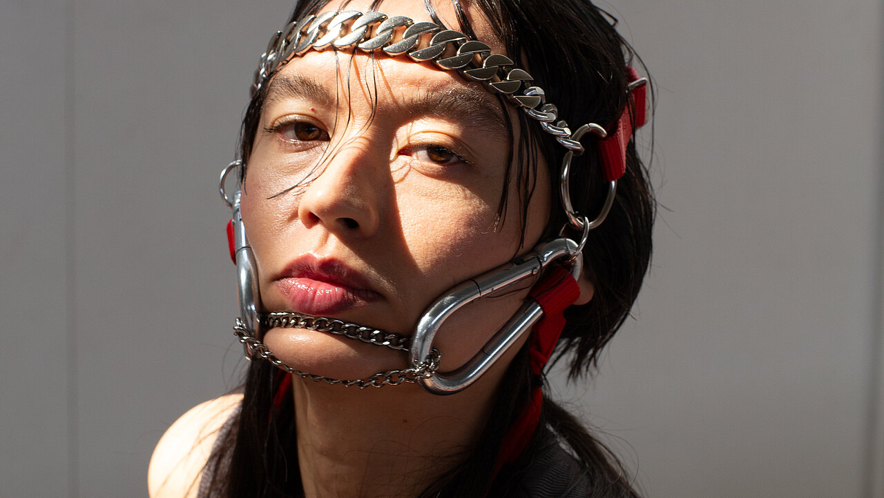 Portrait of Marika Peura, wearing a mask made of chains and carabiners