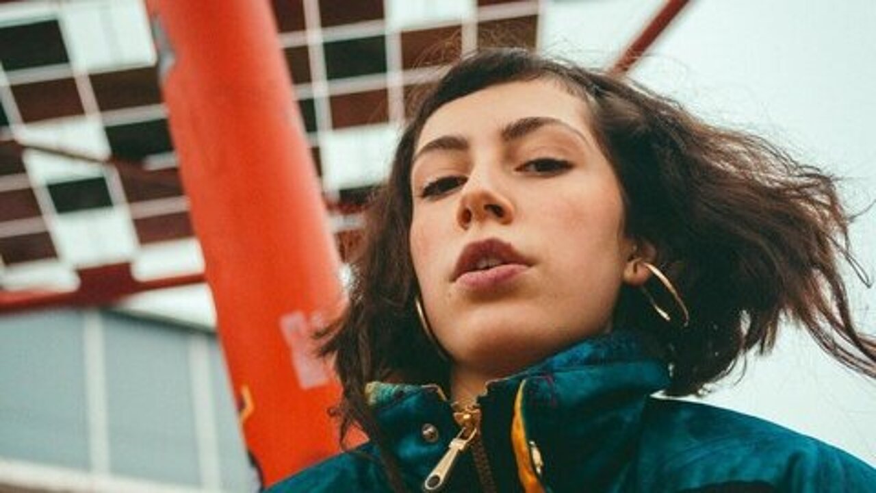 Maira in front of a red geometrical structure, shot frow below