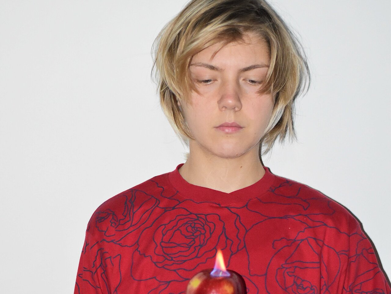 Eliza_Trefas in a red jumper, holding a burning apple in her left hand in front of her heart.