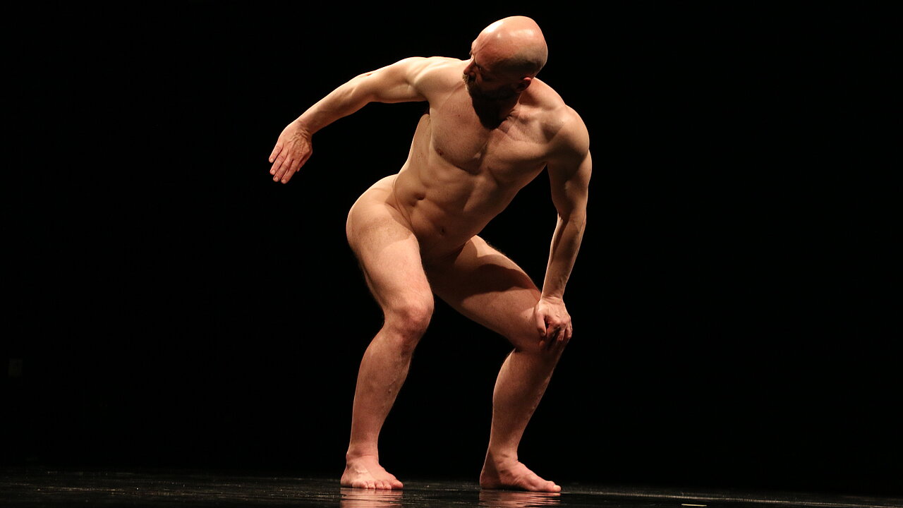 Svetozar Adamović, standing naked, knees bent a bit, arms with a distance to the body, his head turned to his right as if he tries to see his own butt.