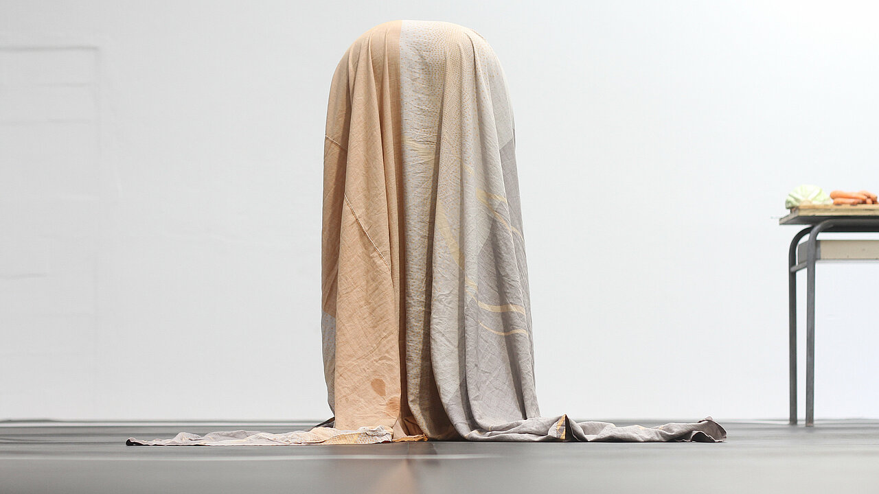 Kaïsha Essiane stending bent forward, complettly hidden underneath a blanket.