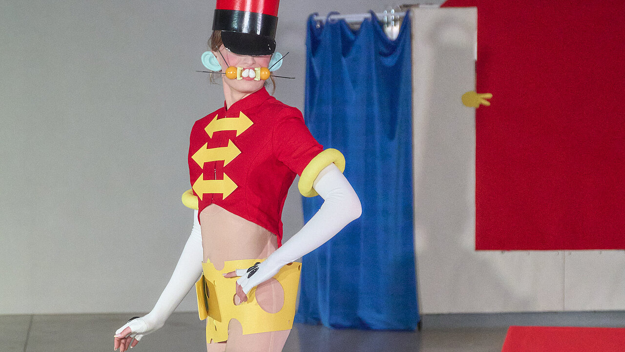 Gabrielle Levie wearing boots up till her thighs, a very long red zylinder hat and a dress which could be of a circus dorector