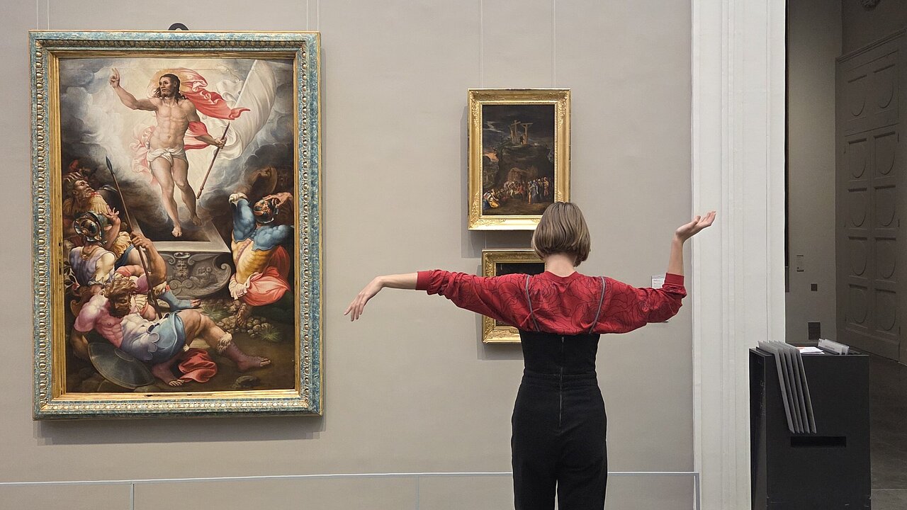 Eliza, seen from behind, standing in front of a painting, imitating the graceful posture