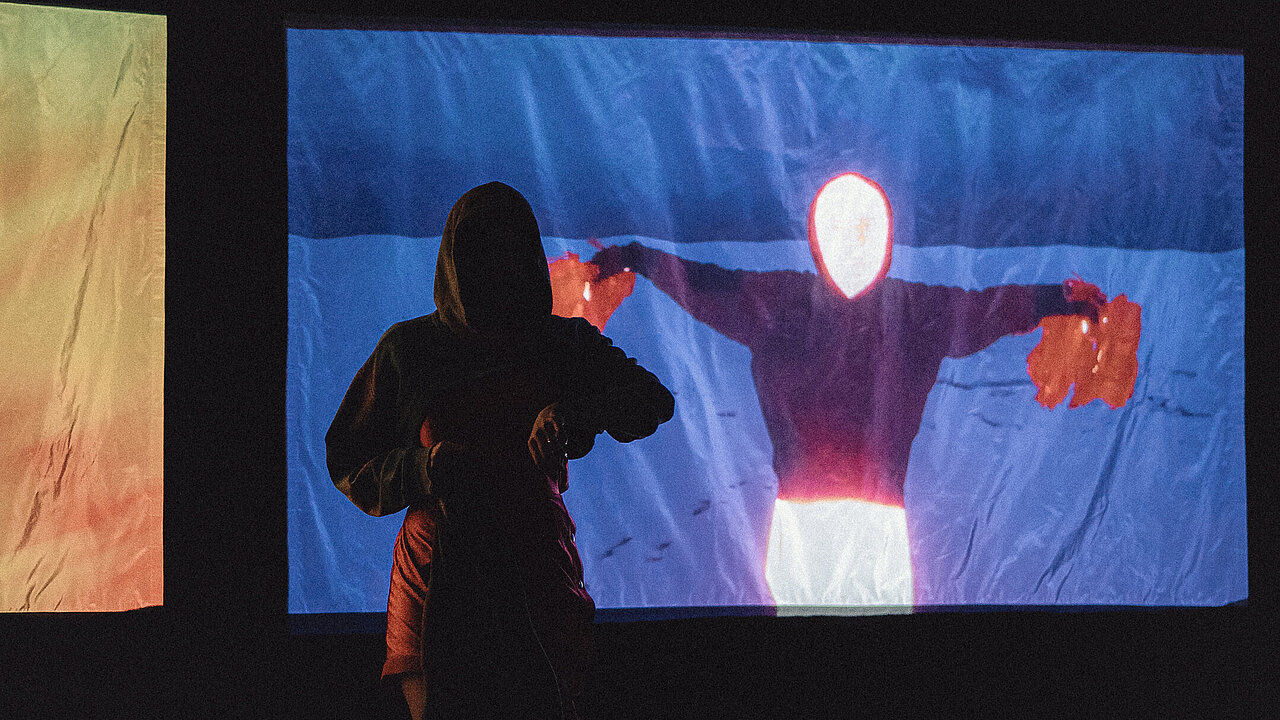 The suíluette of a person in front of a screen, showing a person who's face is not visible, but the area is shining white.