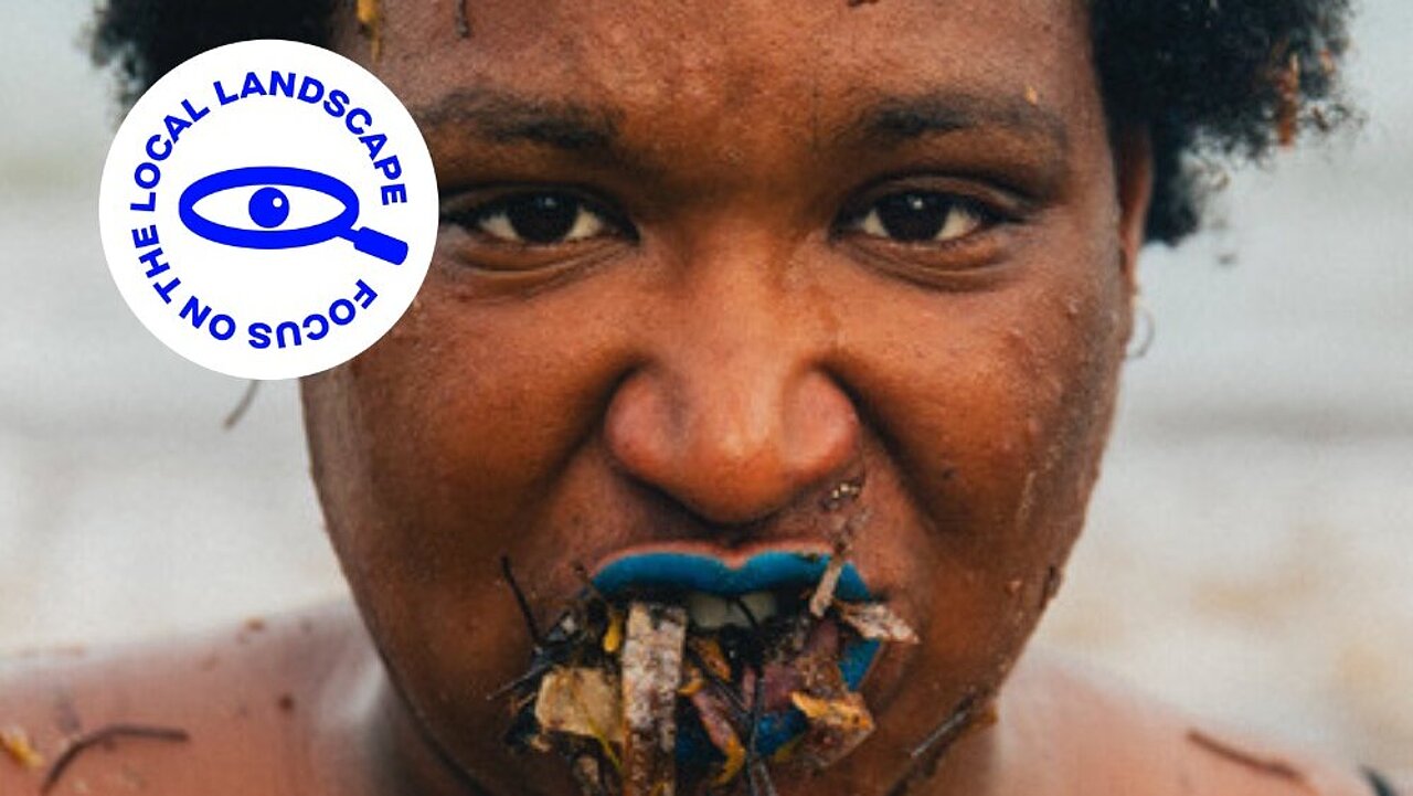 Portrait of Rébecca Chaillon, close up to her face, the mouth full of thinks which poke out of it.