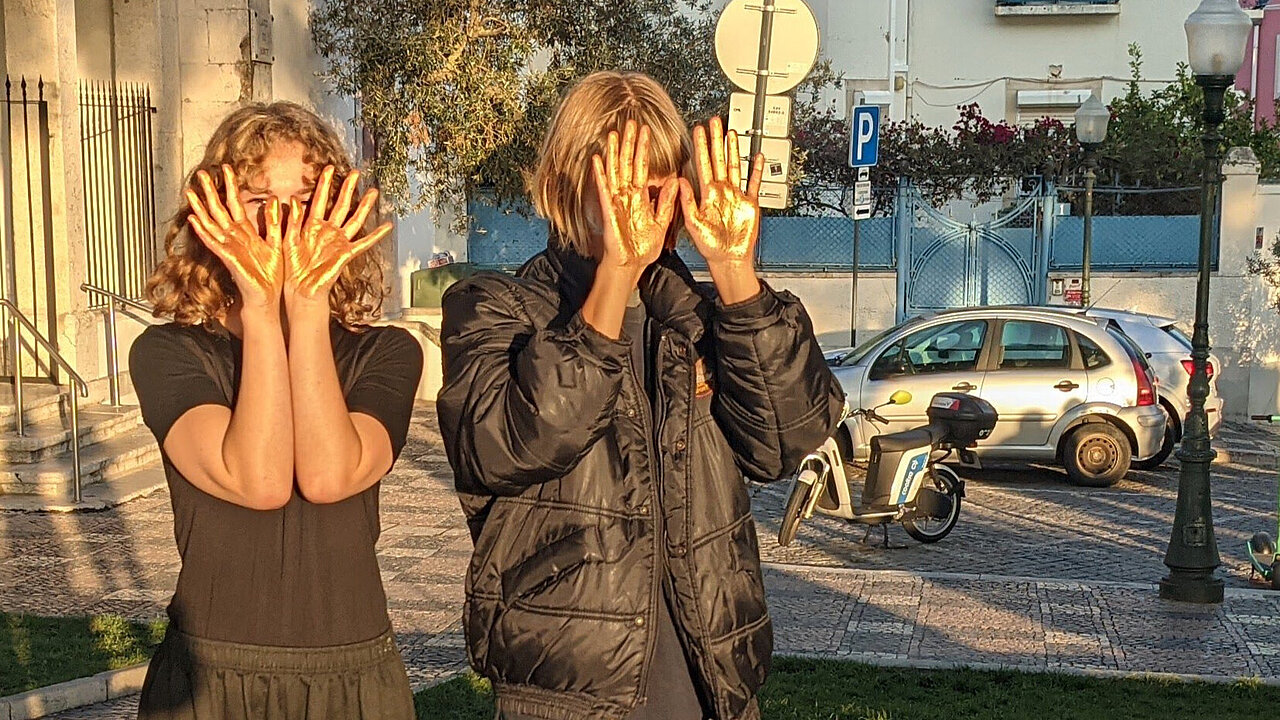 Two women, covering their face with the back of their hands, the inside shining golden.