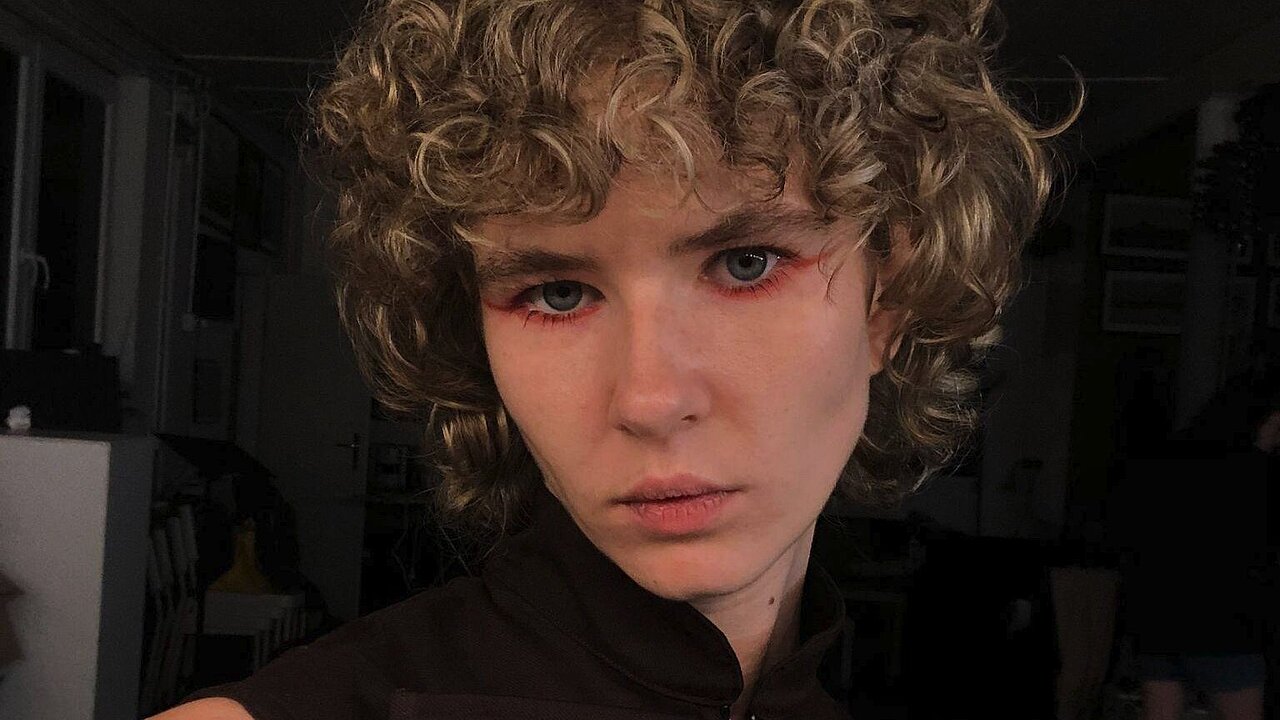 Portrait of Ana Kljujev, blornd curls, black shirt, red eyeliner