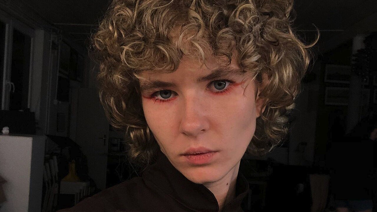Portrait of Ana Kljujev, blornd curls, black shirt, red eyeliner