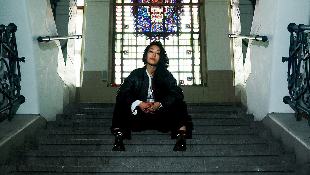 Yoko sitting on stairs a church-like Window in the background