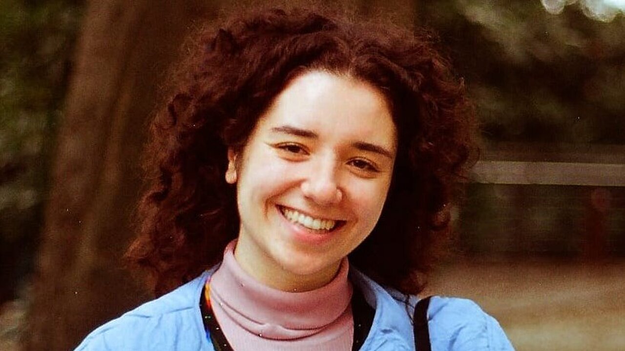Claudia Stoleru in a baby blue jacket, curly open hair, big smile.