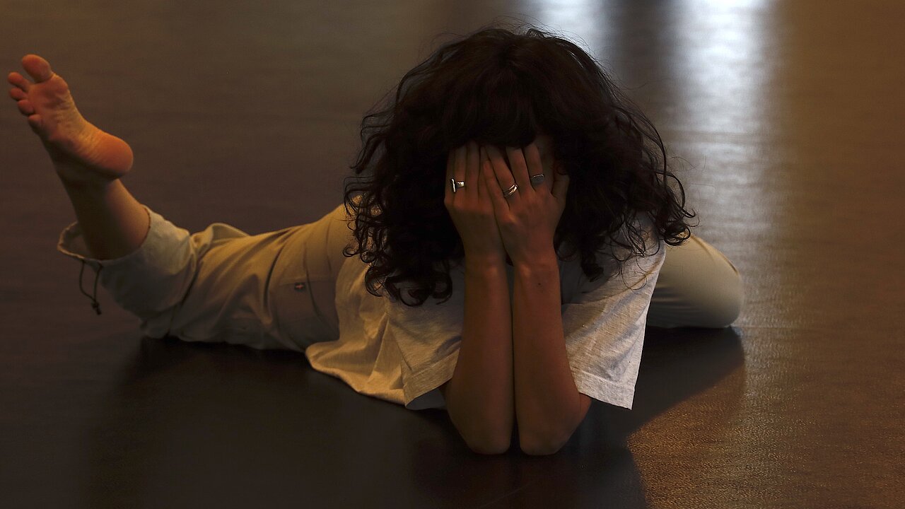 Chen Nadler lying on the floor on her belly, covering her face with both hands,.